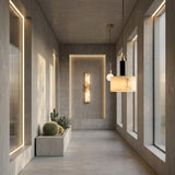 Minimalist hallway with large windows, concrete walls and floors, built-in lighting, a rectangular planter with cacti and succulents, and a Draxen 1 Light Drum Alabaster Single Pendant Light in Soft White & Matte Black.