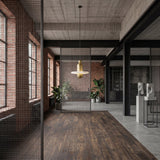 A modern industrial loft with exposed brick walls, big windows, wood floors, metal mesh partitions, potted plants, abstract sculptures, and a Nyxara LED Small Tiered Alabaster Single Pendant Light in Soft White & Gold for a stylish accent.