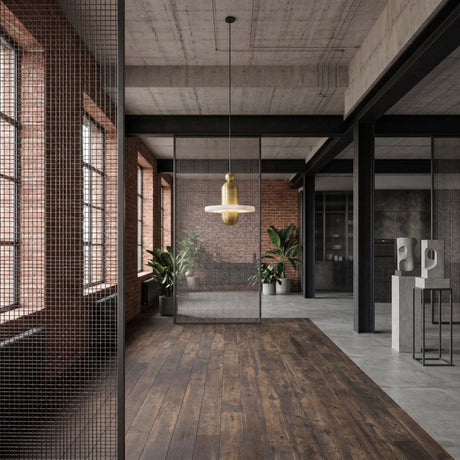 A modern industrial loft with exposed brick walls, big windows, wood floors, metal mesh partitions, potted plants, abstract sculptures, and a Nyxara LED Small Tiered Alabaster Single Pendant Light in Soft White & Gold for a stylish accent.
