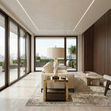 Modern living room with large floor-to-ceiling windows, beige sofa, decorative rug, wooden accent wall, and a city view terrace with plants. Features the Eryndel 1 Light Sculpted Alabaster Table Lamp in brass and soft white for a bright, stylish look.