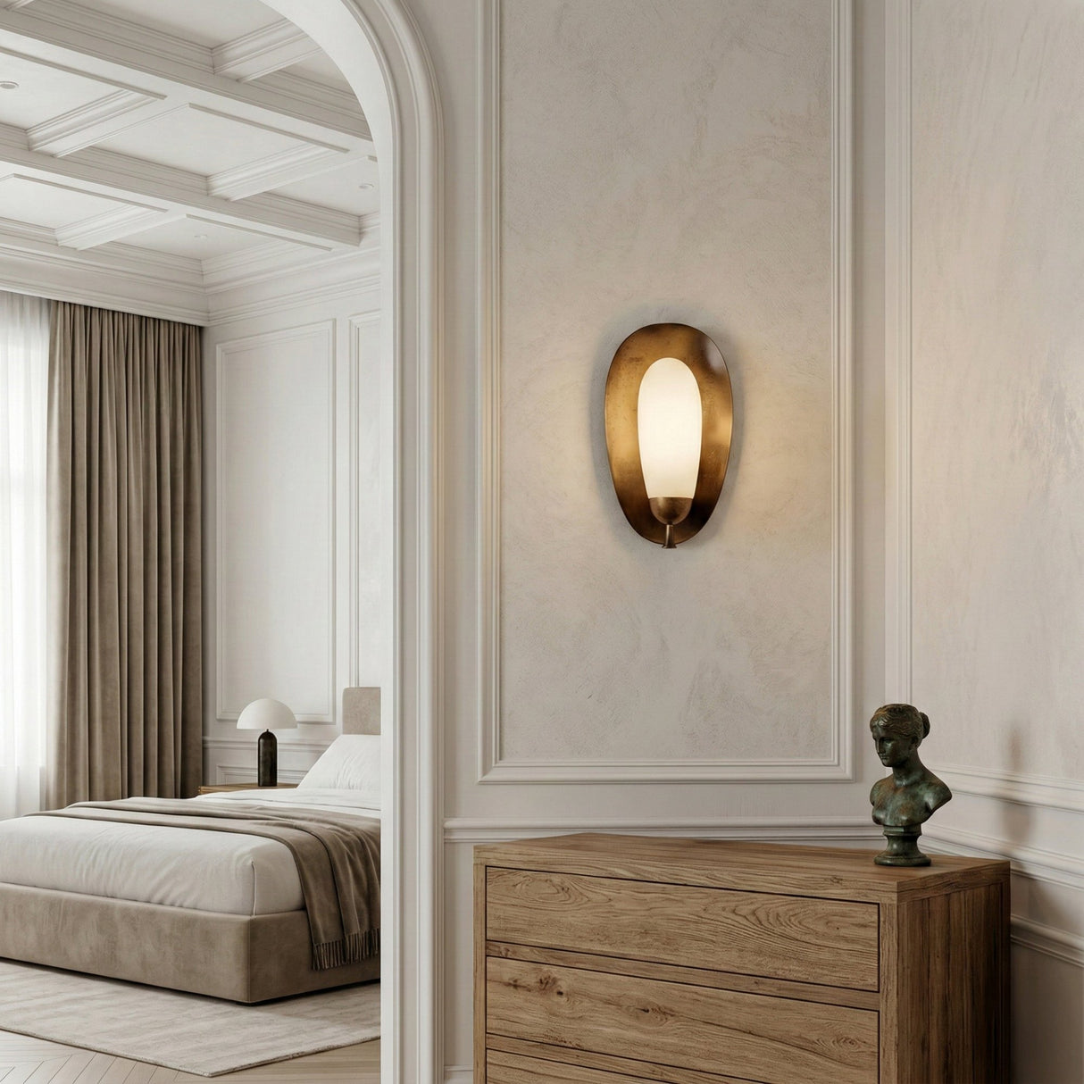 A modern bedroom in neutral tones features a bed by a large window with beige curtains. An Orlisse LED Sculpted Alabaster Wall Light in Soft White & Brushed Bronze adds warm illumination above a wooden dresser.