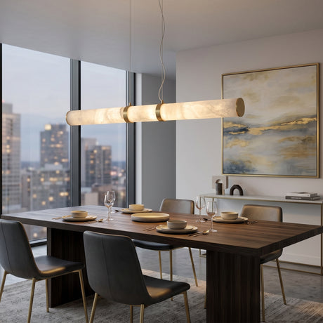 Oria LED Linear Alabaster Chandelier 1m in brass, shown suspended above a dark wood dining table in a modern apartment with city-view windows.