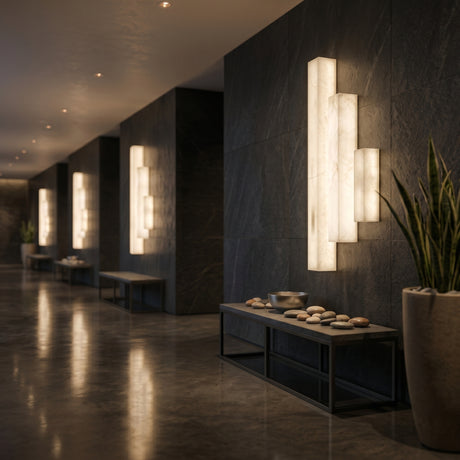 Valmera LED Slim Vertical Alabaster Wall Light in soft white illuminating a dark stone hallway, mounted in a repeating row above wooden benches with stones.