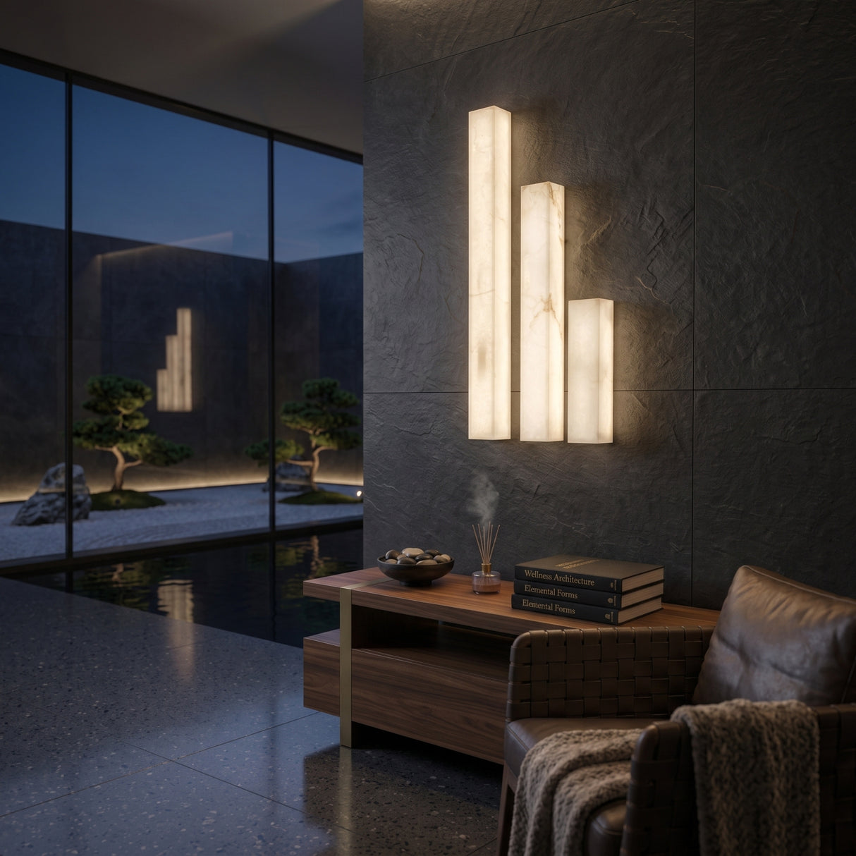 Valmera LED Slim Vertical Alabaster Wall Light in Small size, three staggered rectangular columns glowing warm white on a dark stone wall in a living room setting.