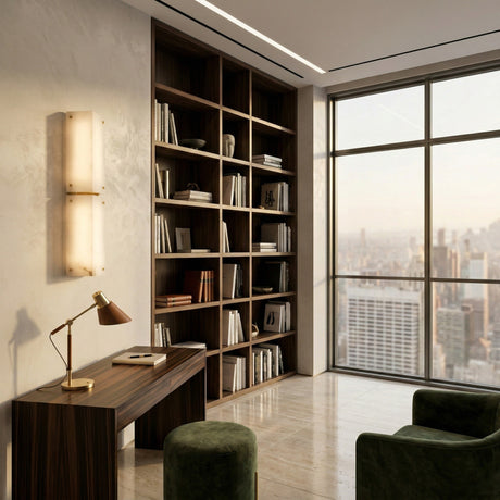 Modern home office featuring a wooden desk, gold lamp, green velvet chairs, built-in bookshelves, and city views. The Auralis 2 Light Double Alabaster Wall Light in Soft White adds elegance to the serene, neutral-toned space.