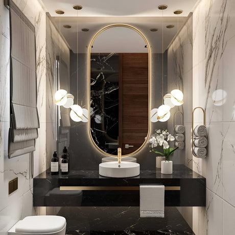 Luxurious bathroom with marble walls, black marble vanity, oval mirror with brass trim, Arc Pendant Light in gold & white, vessel sink, rolled towels, two bottles, and a potted orchid create a refined contemporary design.