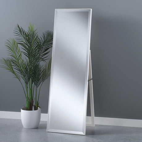 The Empyra Free Standing Mirror in white (153x47x42cm) rests at an angle on a gray-cement floor against a gray wall, with a potted green plant featuring long fronds positioned to the left.