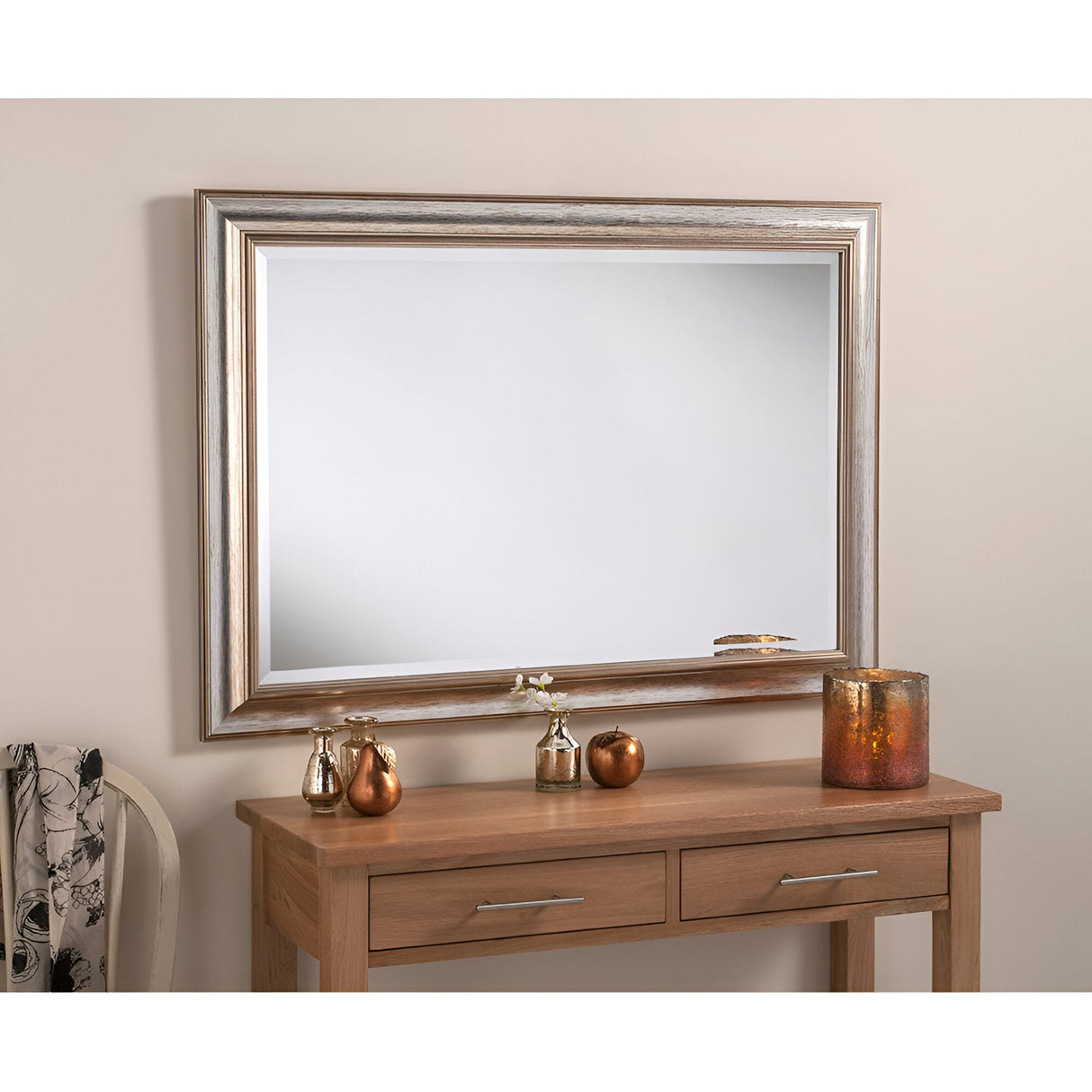 The wooden console table, an elegant home decor piece, boasts two drawers and is beautifully accented with metallic vases. Positioned above the table, the Aris Rectangle Wall Mirror - Silver enhances the ambiance with its sophisticated silver wood frame. A draped patterned fabric nearby completes the charming ensemble.
