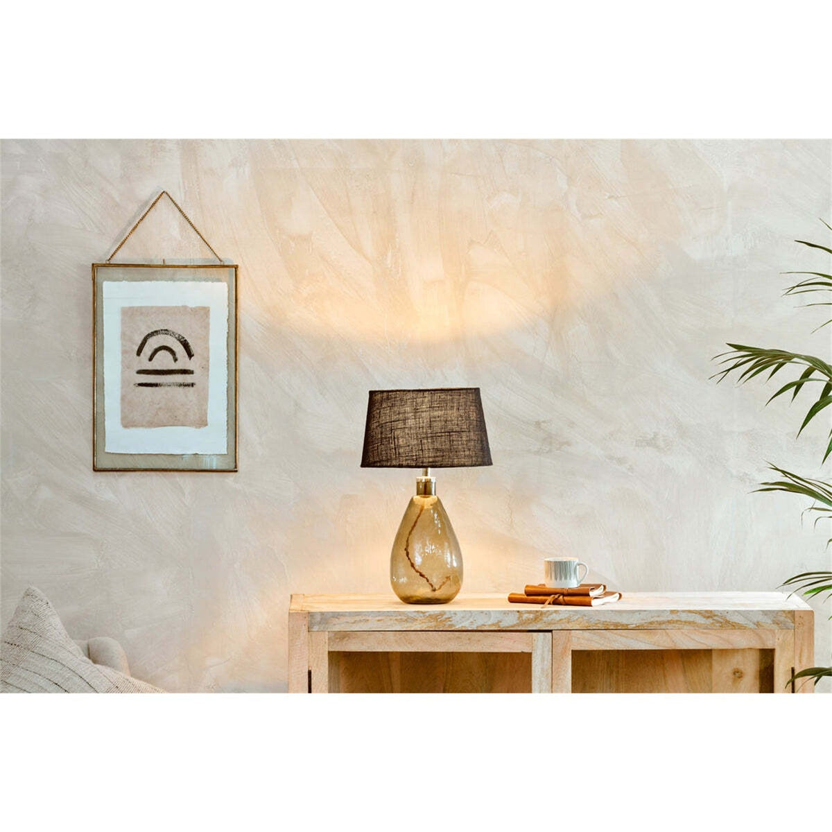 Baba Small Tall Recycled Glass Lamp Base in green with a black fabric shade, styled on a wooden sideboard beside books and a mug in a living room setting.