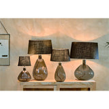 Green teardrop-shaped recycled glass lamp base with hammered texture and chrome collar, shown among taller lamp bases with black shades on a wooden console.