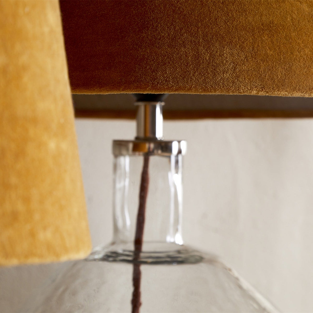 Close-up of the Batakha medium tapered drum lampshade in dark ochre velvet, fitted to a glass table lamp base with chrome gallery, pale linen lining visible at the rim.