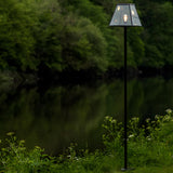 Contemporary Galvanised Steel Lamp Post 2.7m in black with tapered glass lantern shade and lit bulb, standing beside a garden lake edged with greenery.