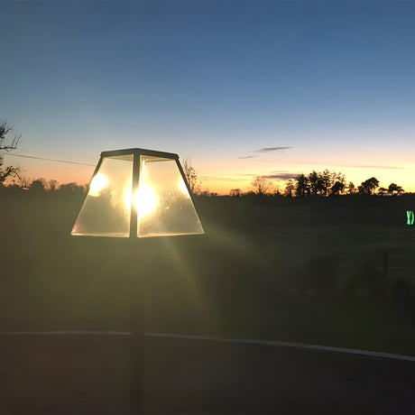 Contemporary Galvanised Steel Lamp Post 1.8m in black with tapered glass lantern head, backlit by sunset in an outdoor garden setting with trees and open sky.