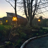 Contemporary black galvanised steel lamp post, 1.8m, with tapered glass-panelled lantern head, shown lit in a garden border at dusk.