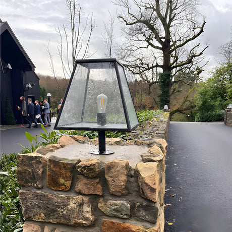 Large Contemporary Pillar Light in black steel with tapered glass shade and exposed bulb, mounted on a stone pier along an outdoor driveway.