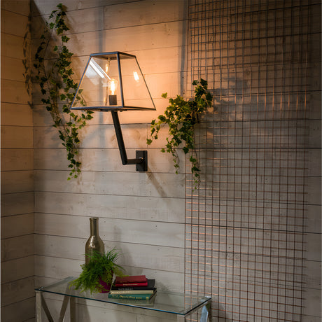 Large Contemporary Wall Lantern in black steel and glass on an angled bracket, mounted on a wood-panelled wall amid trailing ivy, lit and shown above a console table.