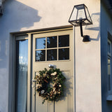 Small contemporary black outdoor wall lantern with tapered glass panels and exposed bulb, mounted on an angled bracket beside a front door.
