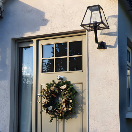 Small contemporary black outdoor wall lantern with tapered glass panels and exposed bulb, mounted on an angled bracket beside a front door.