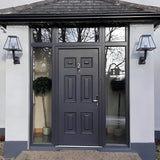 Small contemporary black wall lantern mounted on an angled bracket beside a front door, with glass panels and steel frame in a modern tapered shape.