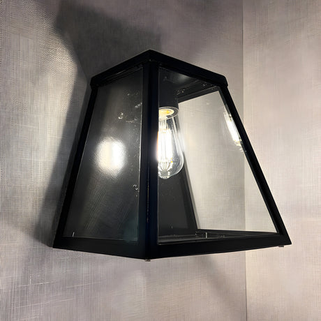 Contemporary Galvanised Steel Bulkhead Wall Light in black, tapered glass panels with visible bulb, mounted against a light grey textured wall.