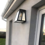 Contemporary Galvanised Steel Bulkhead Wall Light in black, tapered glass design with visible bulb, mounted beside a doorway on a white exterior wall.