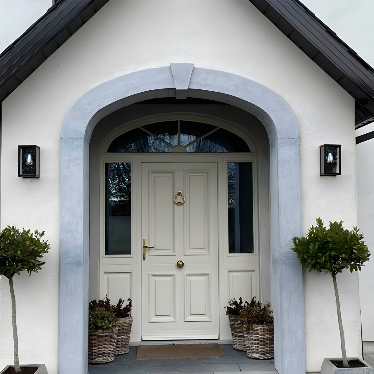 Contemporary Box Wall Lantern in black, a squared single-light outdoor fixture with clear glazing, mounted either side of a white house entrance archway.