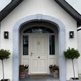 Contemporary Box Wall Lantern in black, a squared single-light outdoor fixture with clear glazing, mounted either side of a white house entrance archway.