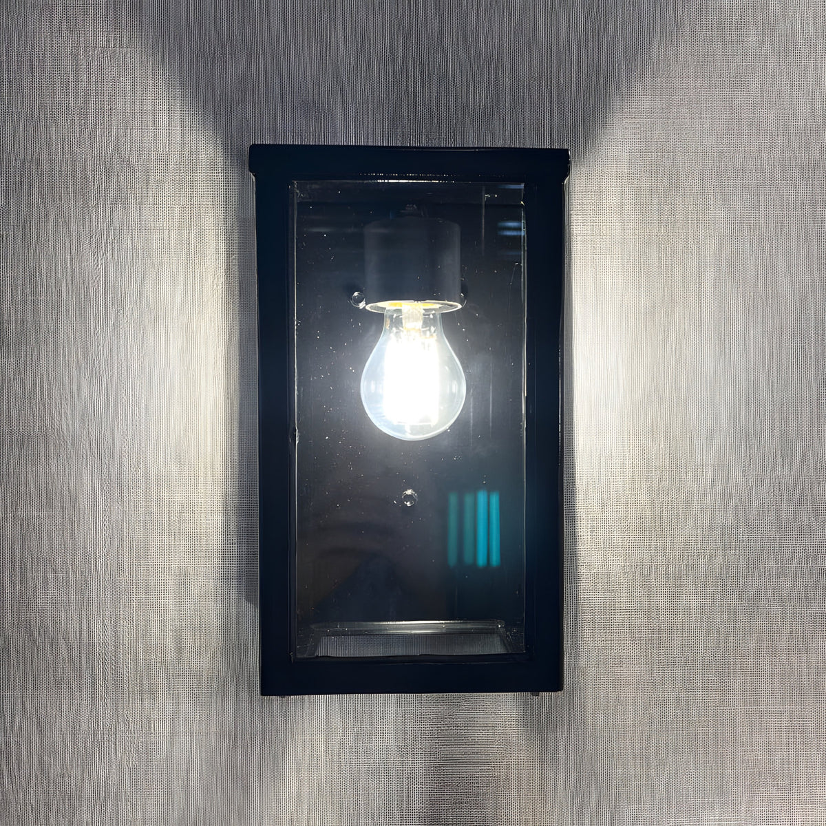 Contemporary Box Wall Lantern in black, a squared steel and glass outdoor fitting with clear glazing showing a single E27 bulb, mounted flat on a textured grey wall.