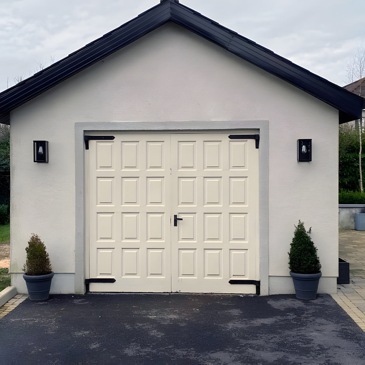 Contemporary Box Wall Lantern in black steel with clear glazing, mounted either side of a garage entrance on a white rendered wall with dark roofline.