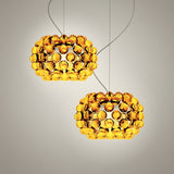 Two Briller LED Small Pendant Lights in gold, each featuring a round amber acrylic sphere, hang by thin wires against a light background, casting a warm golden glow.