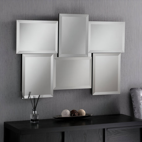 The 112x79cm Verra Rectangle Wall Mirror, made up of six staggered rectangular panels, hangs gracefully on a textured gray wall above a dark wood console table. In this modern bedroom setup, the table is adorned with decorative items such as a reed diffuser and spherical ornaments.
