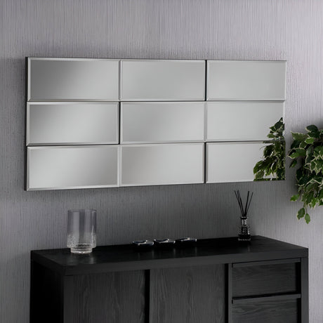 A modern room features a Luxia Rectangle Wall Mirror - 138x62cm, beautifully capturing contemporary design. Positioned horizontally above a dark wooden cabinet, the mirror accentuates three small decorative items and a clear glass vase. A leafy plant elegantly cascades from the side, adding a hint of greenery.