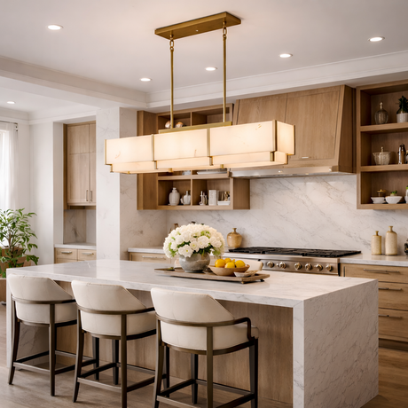 A modern kitchen features light wood cabinets, marble countertops, a large island with three upholstered chairs, and the Albyso LED Linear Alabaster Chandelier in brushed brass & soft white, plus vases and bowls of white flowers and lemons.