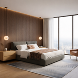 A modern bedroom with a gray upholstered bed, wooden slat accent wall, two wooden nightstands topped with Novara 1 Light Globe Alabaster Single Pendant Lights in Soft White, a patterned rug, pink chair, and floor-to-ceiling windows overlooking the city.