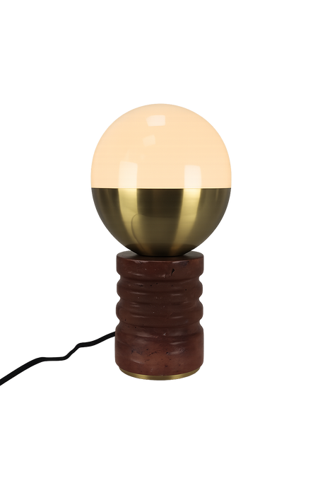 The Caldris 1 Light Sculpted Marble Table Lamp in Brass & Dark Terracotta Red features a round, half-glass, half-brass shade atop a textured cylindrical base with a black electrical cord.