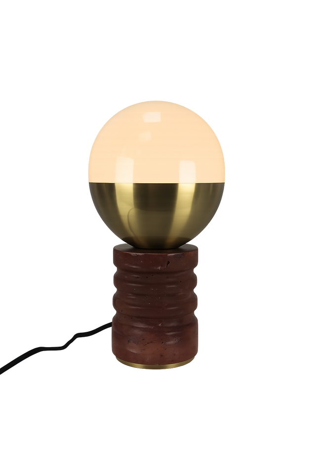 The Caldris 1 Light Sculpted Marble Table Lamp in Brass & Dark Terracotta Red features a round, half-glass, half-brass shade atop a textured cylindrical base with a black electrical cord.