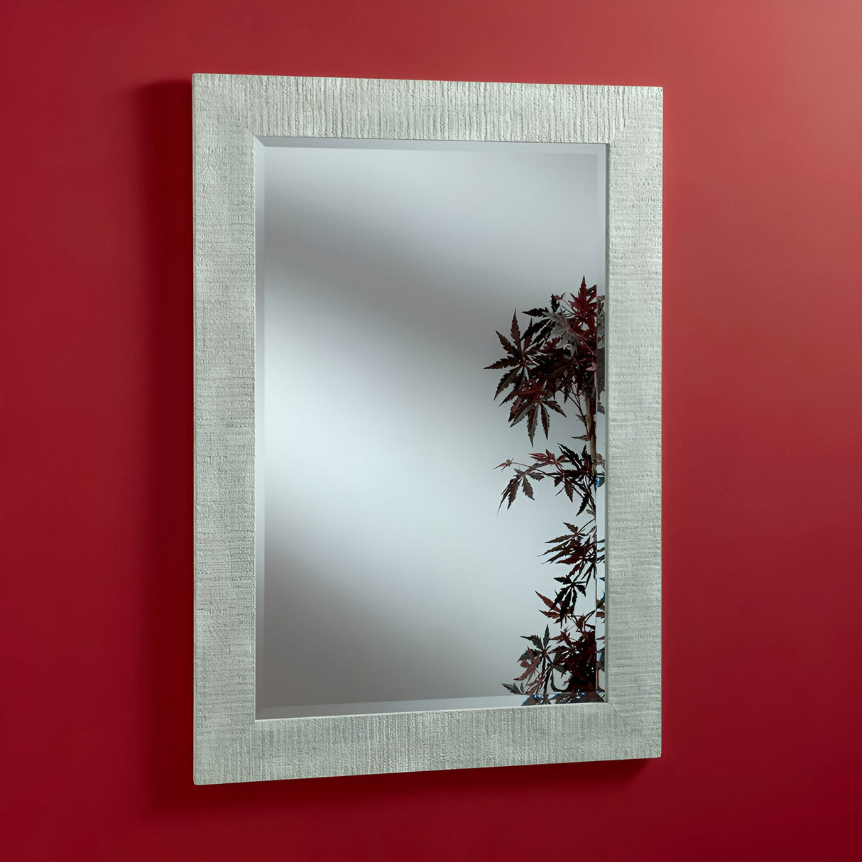 The Zennia Rectangle Wall Mirror in white, featuring a textured silver frame, perfectly elevates your home decor by reflecting red maple leaves against a smooth red wall.