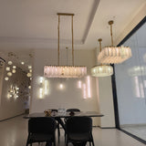 Lunaro linear alabaster chandelier with brushed brass frame and rod suspension, illuminated stone panels shown above a dining table in a showroom setting.