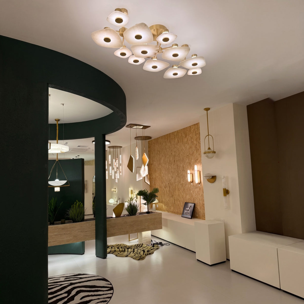 Calyra Large LED Alabaster Semi-Flush Ceiling Light in brass, with twelve layered alabaster panels illuminated warm white, shown mounted above a modern showroom interior.