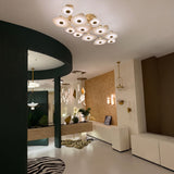 Calyra Large LED Alabaster Semi-Flush Ceiling Light in brass, with twelve layered alabaster panels illuminated warm white, shown mounted above a modern showroom interior.