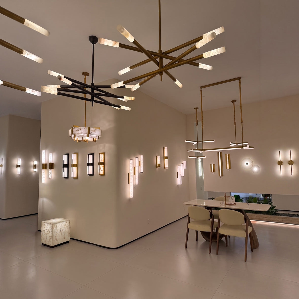 Aurelian LED chandelier with crossed copper arms in satin nickel, each ending in cylindrical alabaster diffusers, shown alongside coordinating wall lights in a showroom setting.