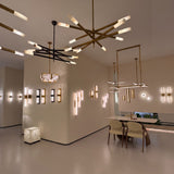 Aurelian LED chandelier with crossed copper arms in satin nickel, each ending in cylindrical alabaster diffusers, shown alongside coordinating wall lights in a showroom setting.