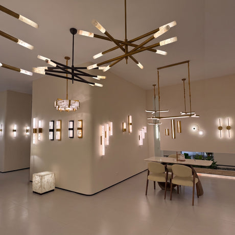 Aurelian LED chandelier with crossed copper arms in satin nickel, each ending in cylindrical alabaster diffusers, shown alongside coordinating wall lights in a showroom setting.