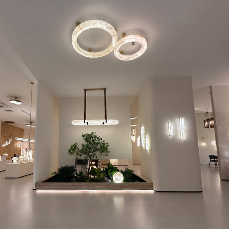 Orbis Extra Large LED Alabaster Semi-Flush Ceiling Light in soft white, two overlapping alabaster rings with brushed brass mounts, shown installed above a showroom display.