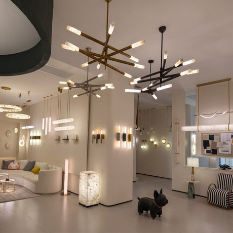 Aurelian LED chandeliers with crossed copper arms in satin nickel finish and cylindrical alabaster diffusers, shown suspended over a showroom seating and display area.