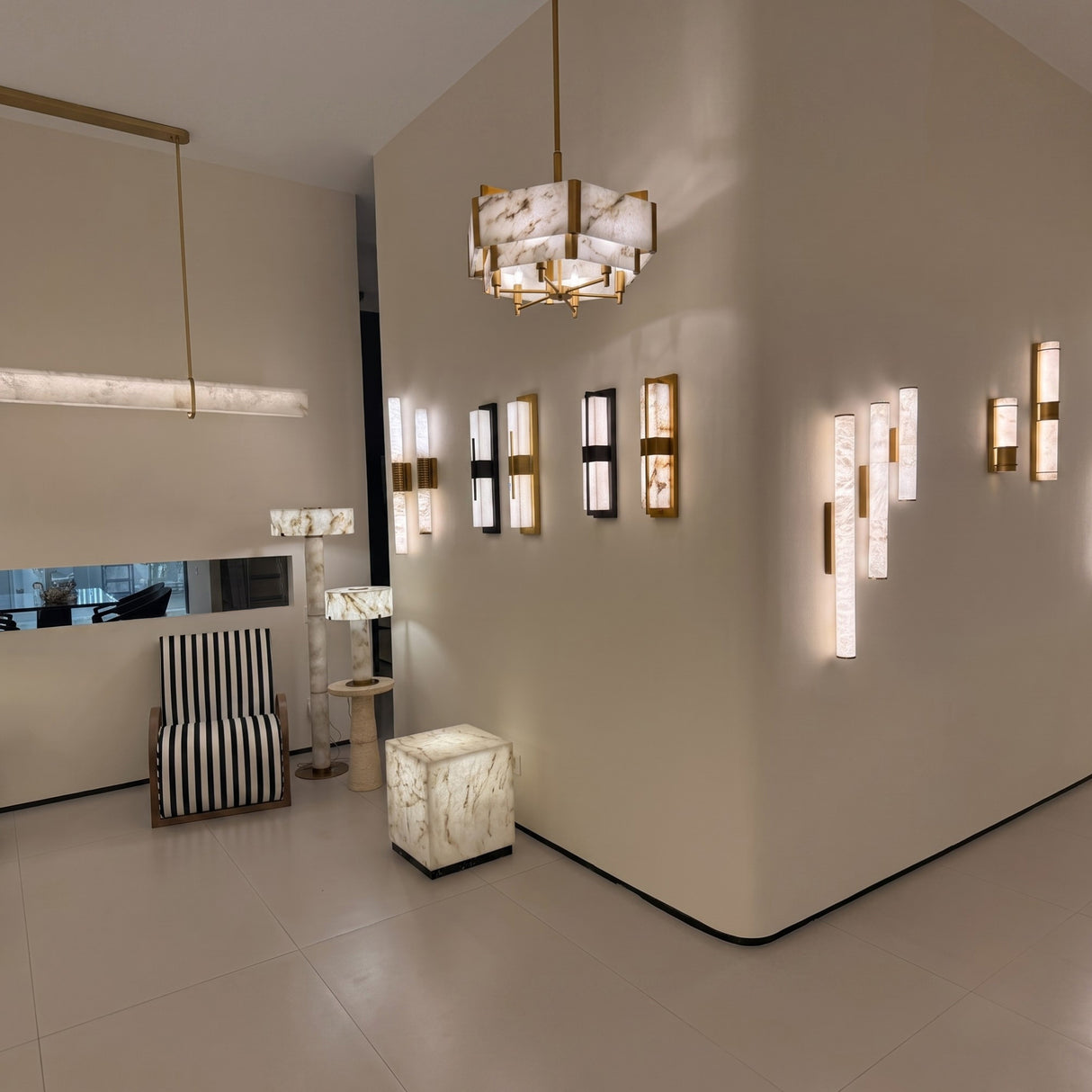 Caldera Large Alabaster Wall Light in matt black, shown among multiple wall lights in a showroom, elongated alabaster panel split by a black metal band with warm integrated LED glow.