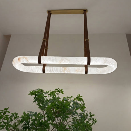 Cintura LED Small Alabaster Floating Pendant Light with oval stone ring, brass ceiling plate and brown leather straps, shown illuminated above a green plant in a neutral room.