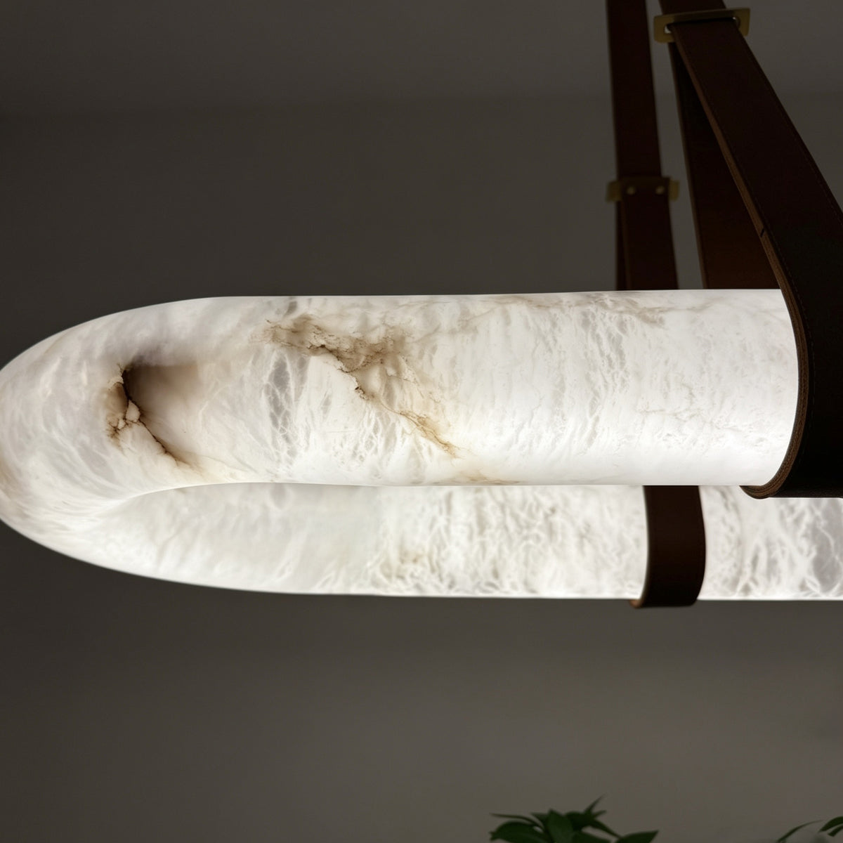 Close-up of the Cintura Small LED alabaster pendant light, showing the oval stone ring's natural veining and leather straps securing it to a copper top bar.