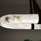 Close-up of the Cintura Small LED alabaster pendant light, showing the oval stone ring's natural veining and leather straps securing it to a copper top bar.