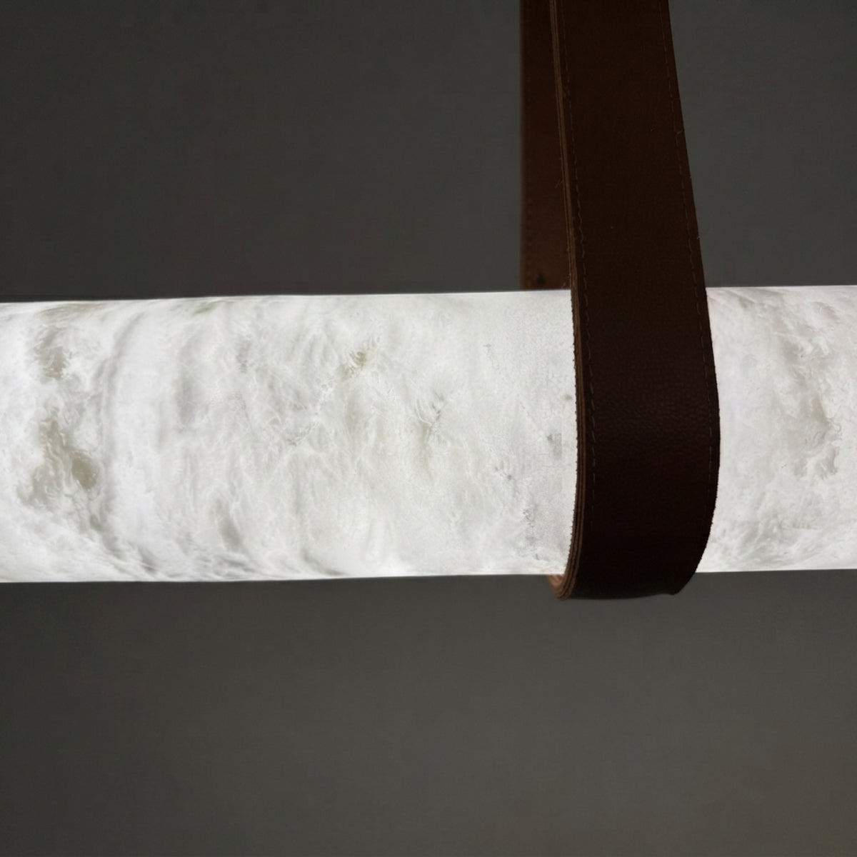 Close-up of the Cintura Small LED alabaster pendant light, showing the textured stone ring and a brown leather strap wrapped over it against a grey background.